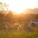 A sunrise in neature while tents are set up for camping with an SUV car next to the tents.