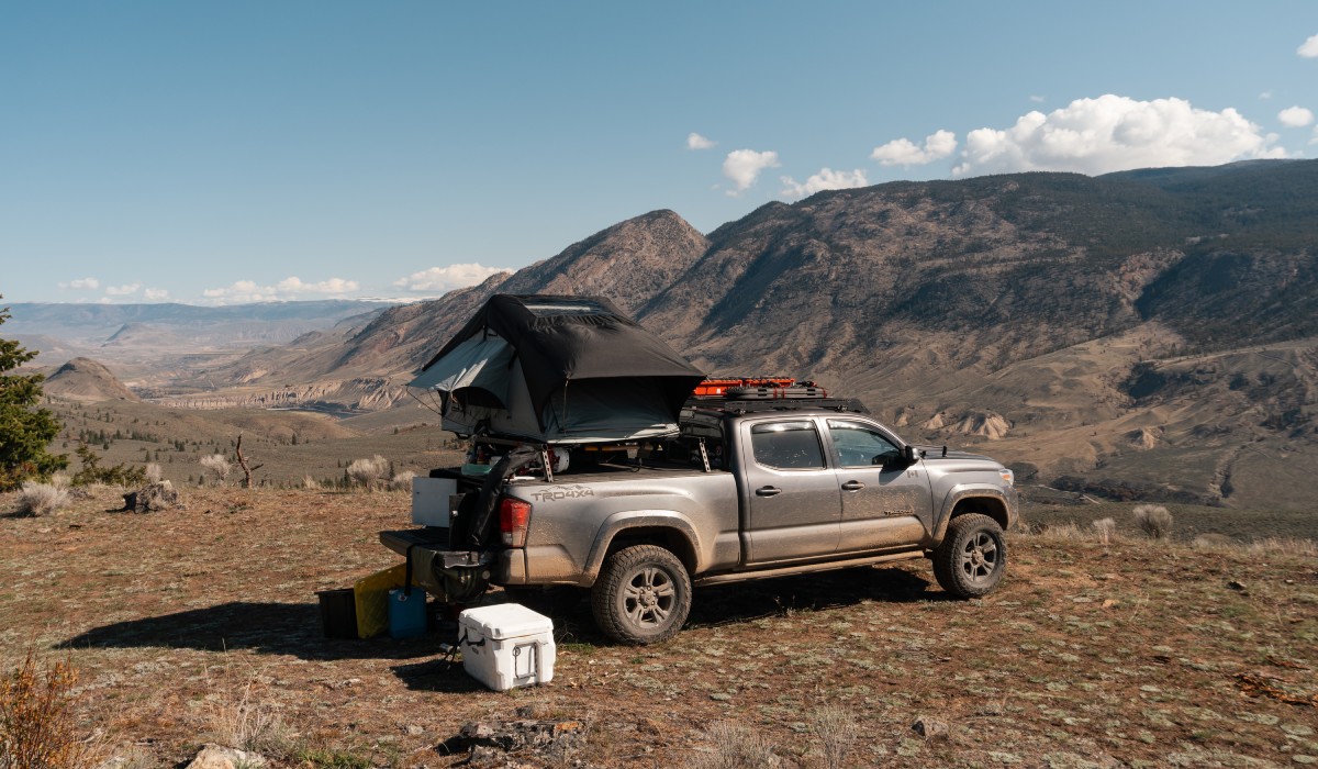 A truck with a pile of equipmen tin the bed is parked on a patch of dirt. In the distance are barren mountains.
