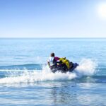 A rookie jet skier out on the water alone. They turn their ski, creating a wake in the water, while wearing a safety vest.